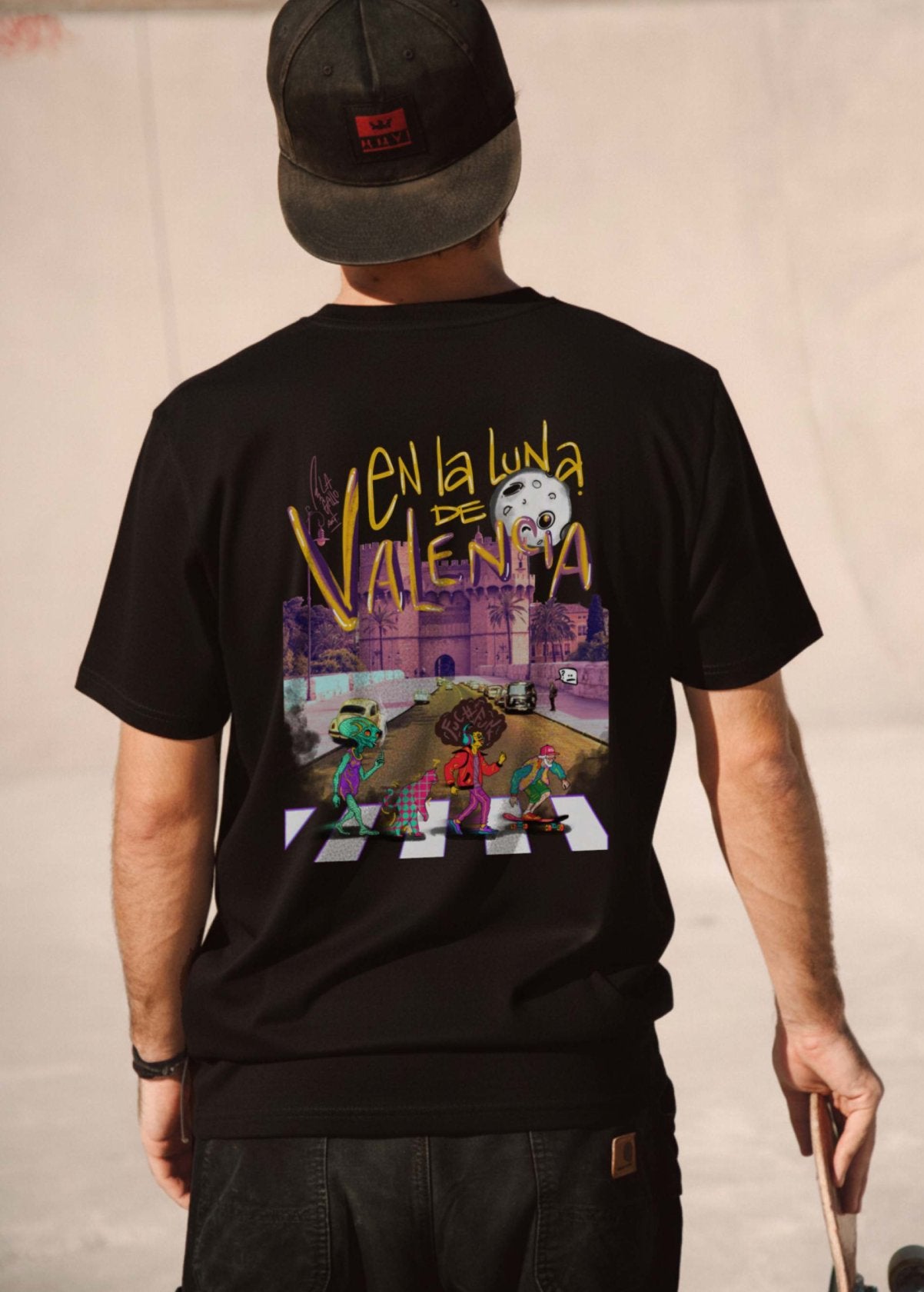 Hombre con camiseta unisex “En la luna de Valencia” negra, vista de espalda. Diseño artístico impreso en algodón orgánico de alta calidad.