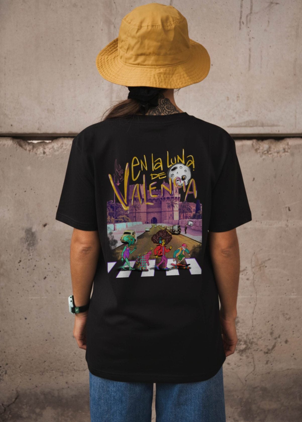 Mujer con camiseta unisex “En la luna de Valencia” negra, vista de espalda. Arte digital independiente impreso en algodón ecológico.