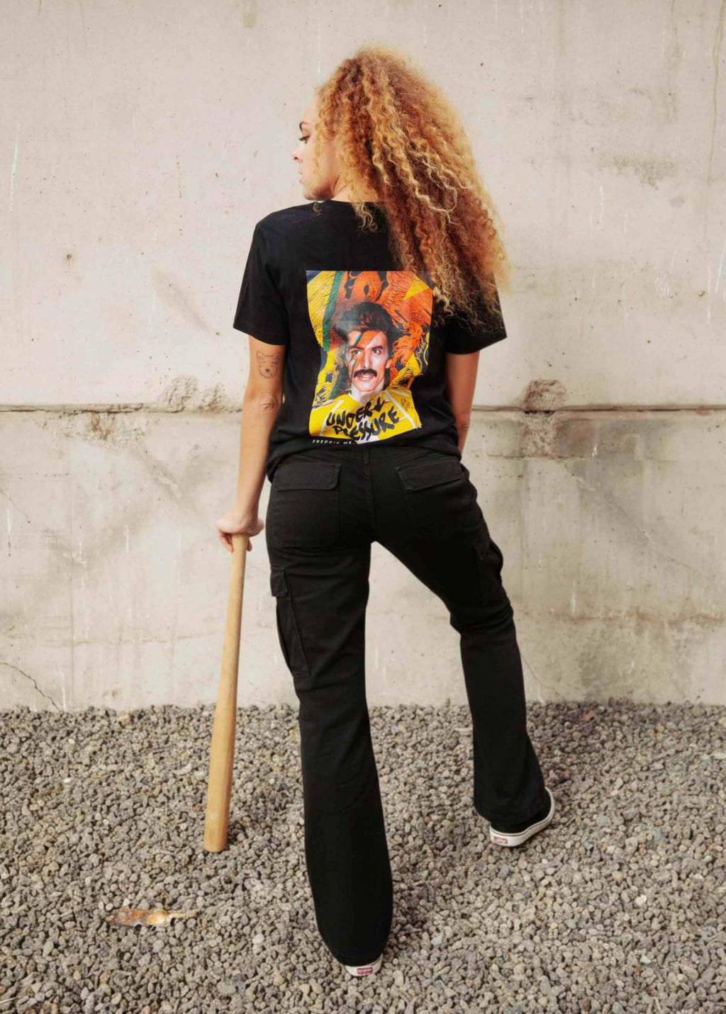 Mujer con camiseta unisex “Freddie Bowie” negra, vista de espalda con diseño “Under Pressure”. Arte digital independiente LA GALLO ART.