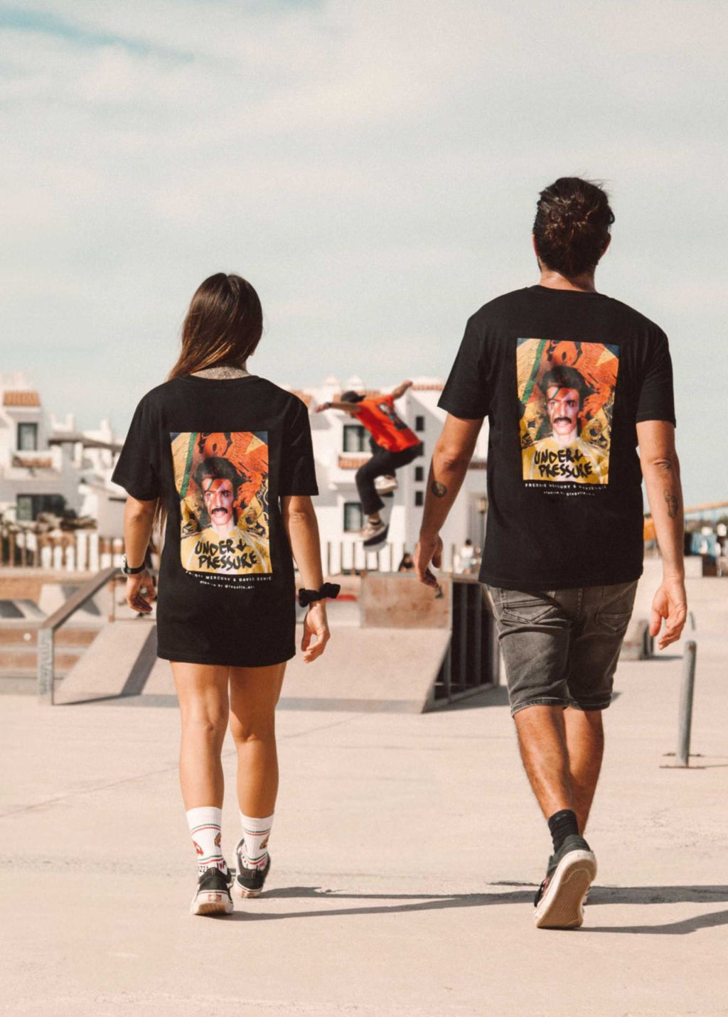 Pareja de modelos unisex con camiseta “Freddie Bowie” negra, vista de espalda. Fusión artística de Freddie Mercury y David Bowie.