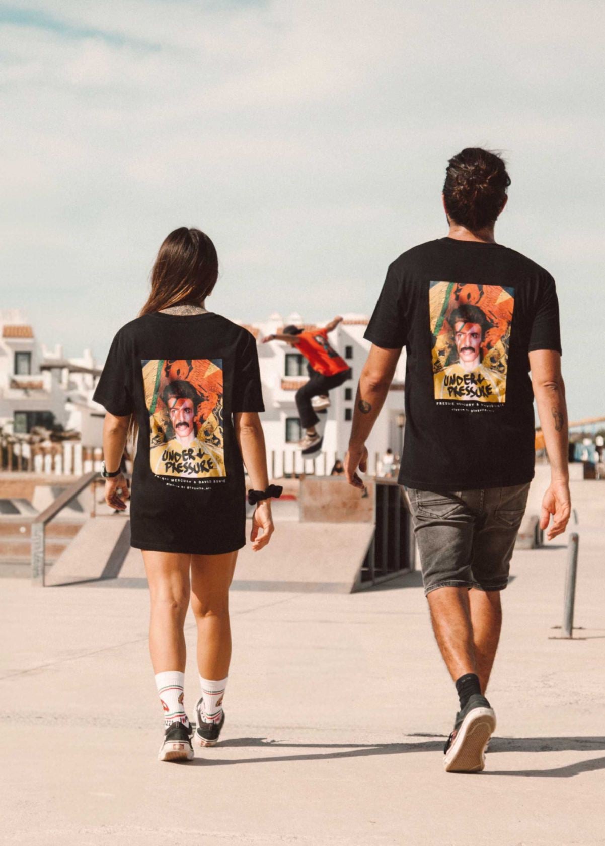 Pareja de modelos unisex con camiseta “Freddie Bowie” negra, vista de espalda. Fusión artística de Freddie Mercury y David Bowie.