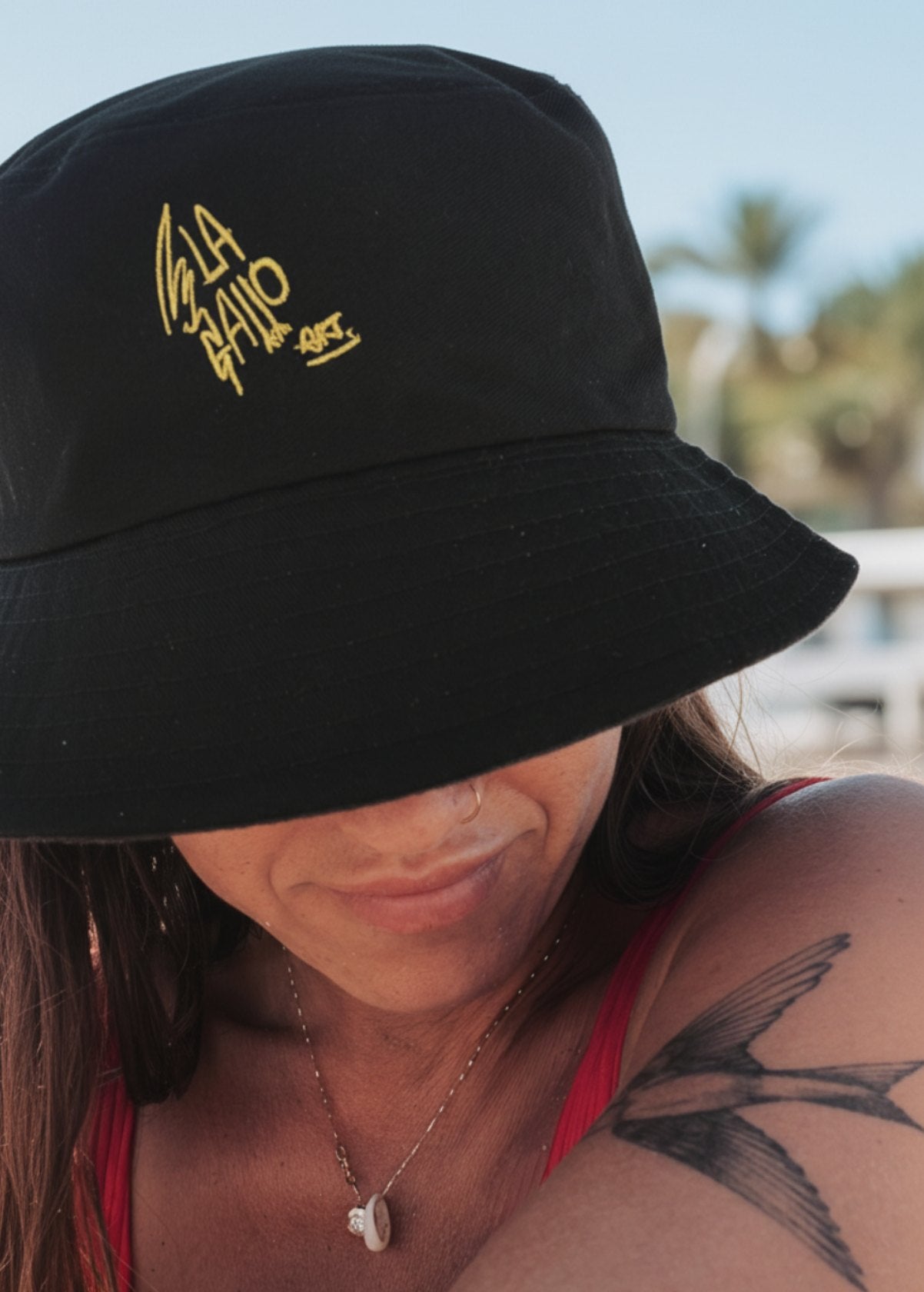 Gorro bucket negro LA GALLO ART en modelo mujer, logo bordado amarillo, estilo urbano en exterior.
