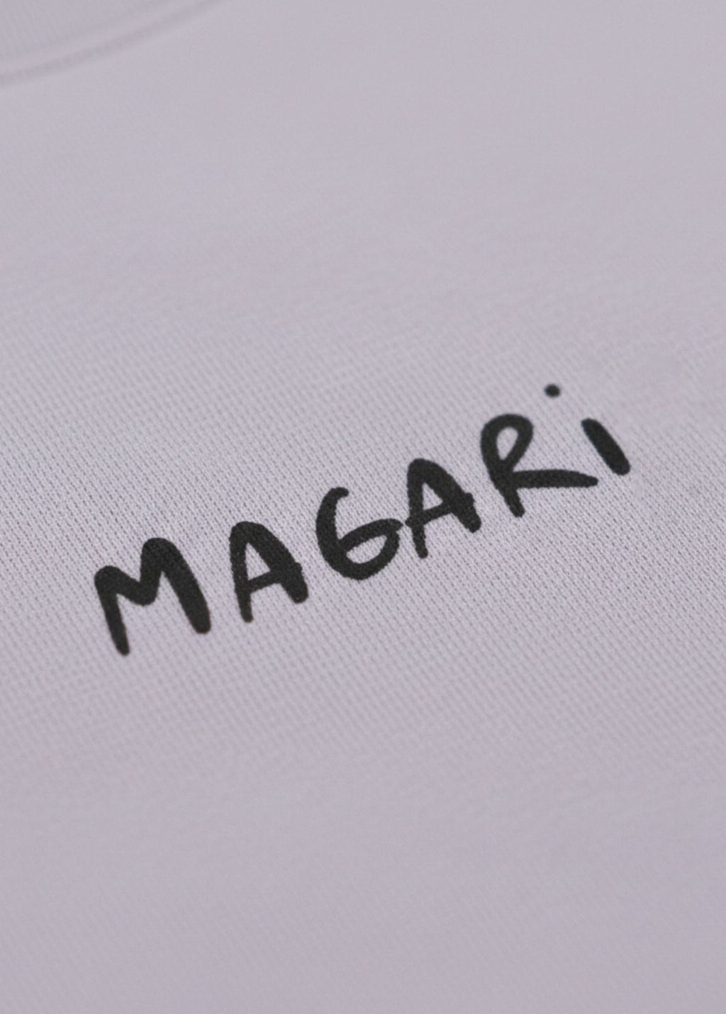 Detalle frontal del diseño “Magari” en camiseta color Lavender. Textura y acabado de impresión artística.