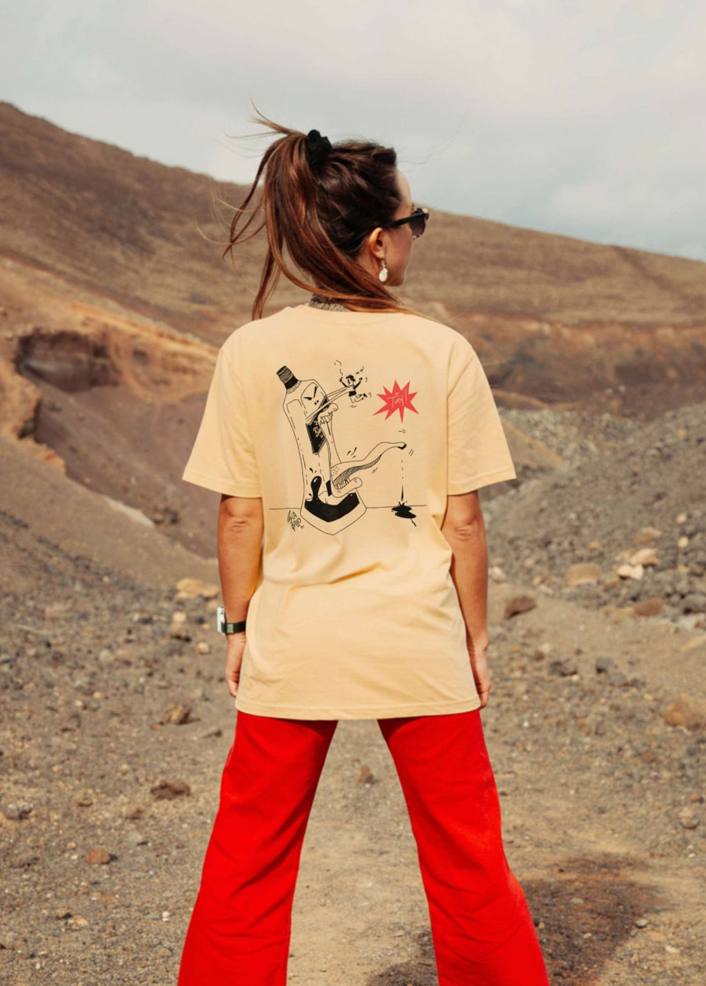 Mujer con camiseta unisex “Whisky” color Níspero, vista de espalda. Arte digital impreso en algodón ecológico.